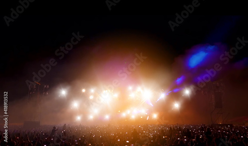 Crowd of people in concert festival against spotlight and smoke.