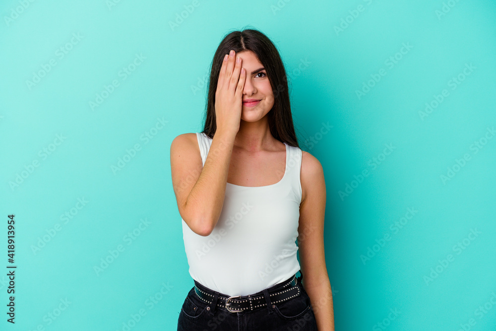 Young caucasian woman isolated on blue background having fun covering half of face with palm. Young caucasian woman isolated on blue background having fun covering half of face with palm.