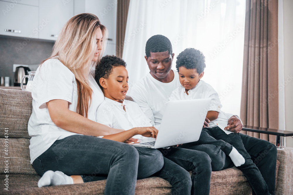 Multiracial family is together at home at daytime watching movie on laptop Multiracial family is together at home at daytime watching movie on laptop