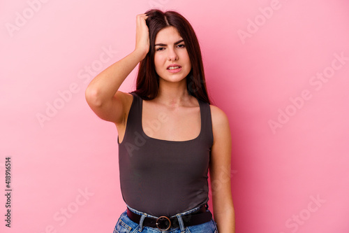 Young caucasian woman isolated on pink background forgetting something  slapping forehead with palm and closing eyes.