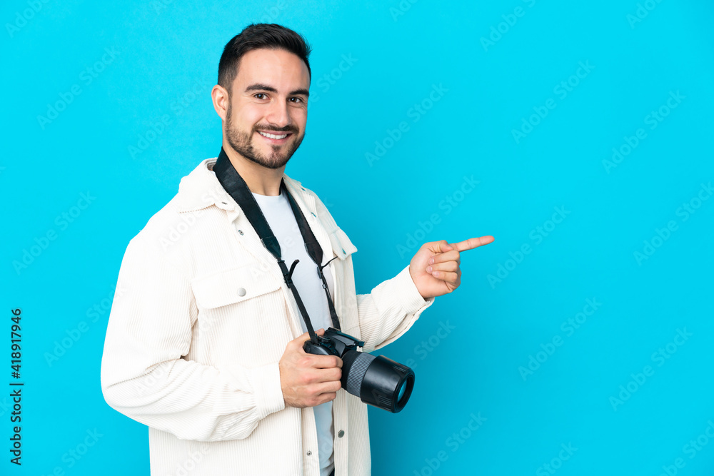 Young photographer man isolated on blue background pointing finger to the side