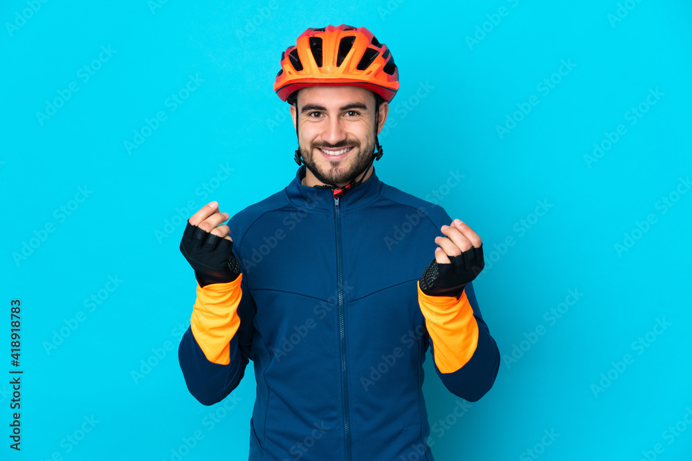 Young cyclist man isolated on blue background making money gesture - obrazy, fototapety, plakaty 