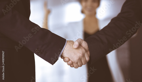 Unknown businesspeople are shaking their hands after signing a contract, while standing together in a modern office, close-up. Business communication, handshake, and marketing concept