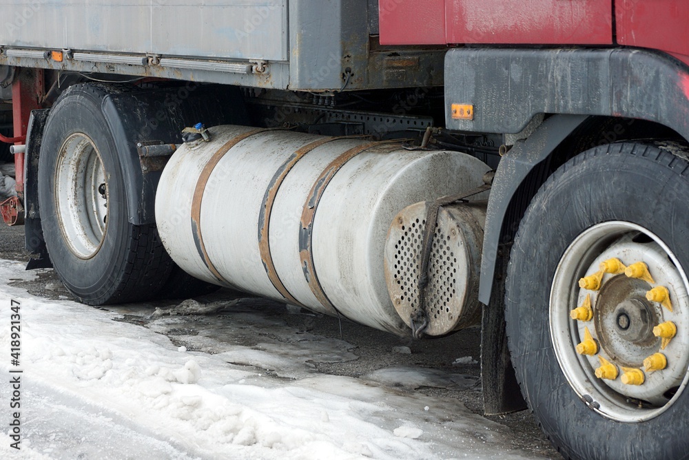 part of a truck with a large gray iron gas tank and black wheels stands on white snow on a winter street part of a truck with a large gray iron gas tank and black wheels stands on white snow on a winter street