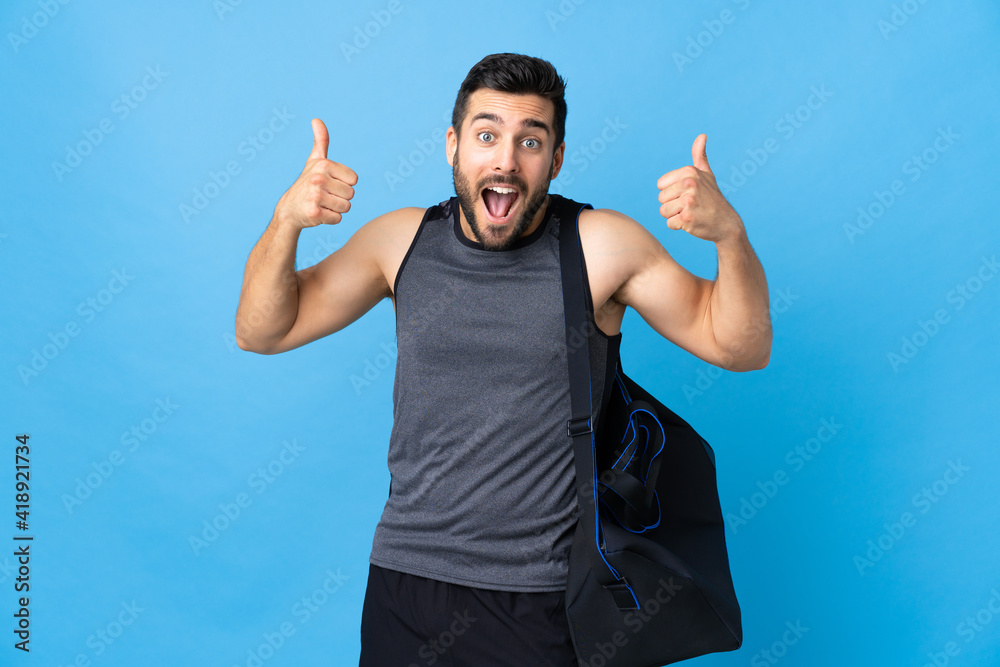 Young sport man with sport bag isolated on blue background giving a thumbs up gesture Young sport man with sport bag isolated on blue background giving a thumbs up gesture