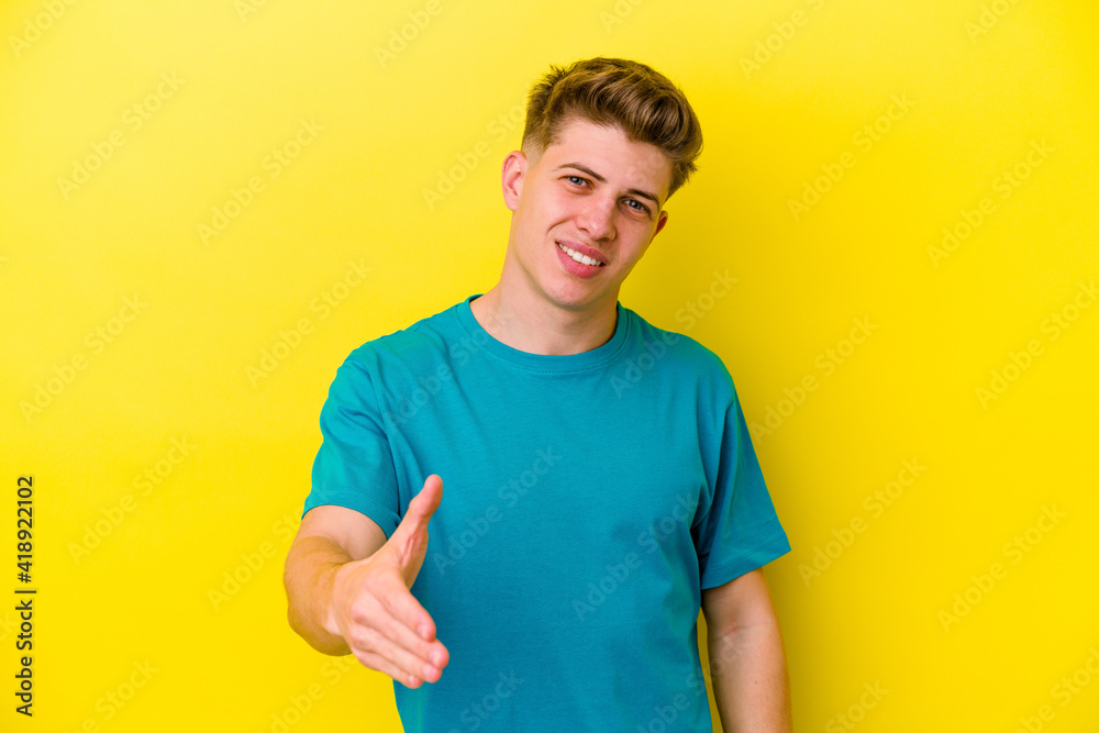 Young caucasian man isolated on yellow background stretching hand at camera in greeting gesture.