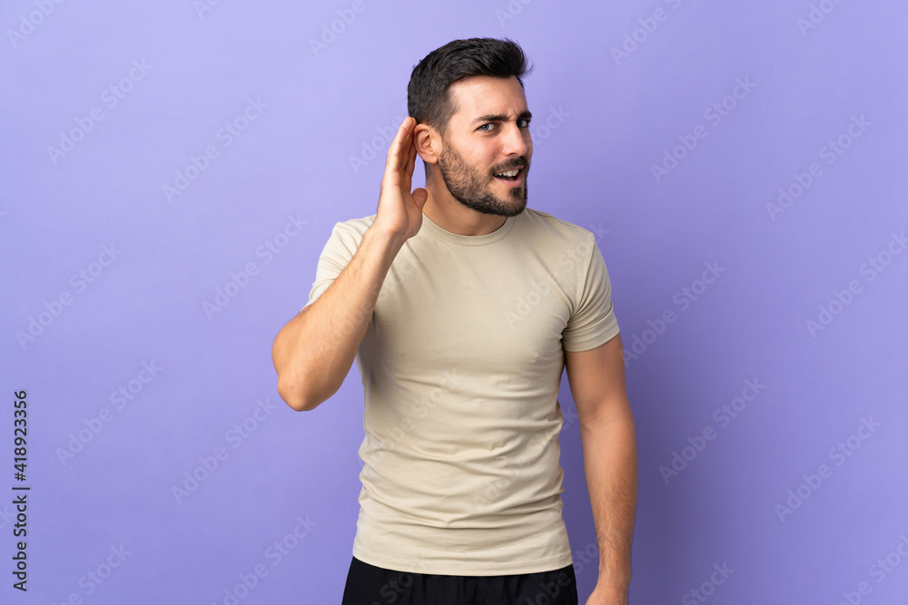 Young handsome man with beard over isolated background listening to something by putting hand on the ear Young handsome man with beard over isolated background listening to something by putting hand on the ear
