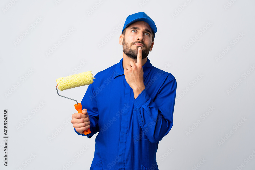 Painter man holding a paint roller isolated on white background having doubts while looking up Painter man holding a paint roller isolated on white background having doubts while looking up