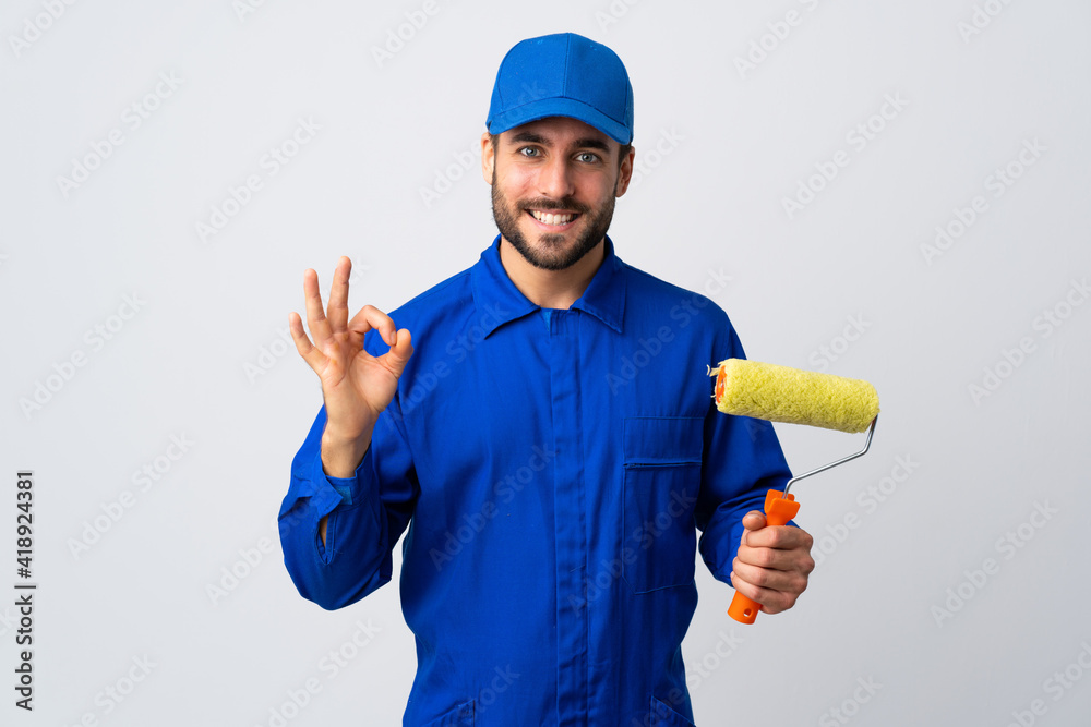 Painter man holding a paint roller isolated on white background showing ok sign with two hands