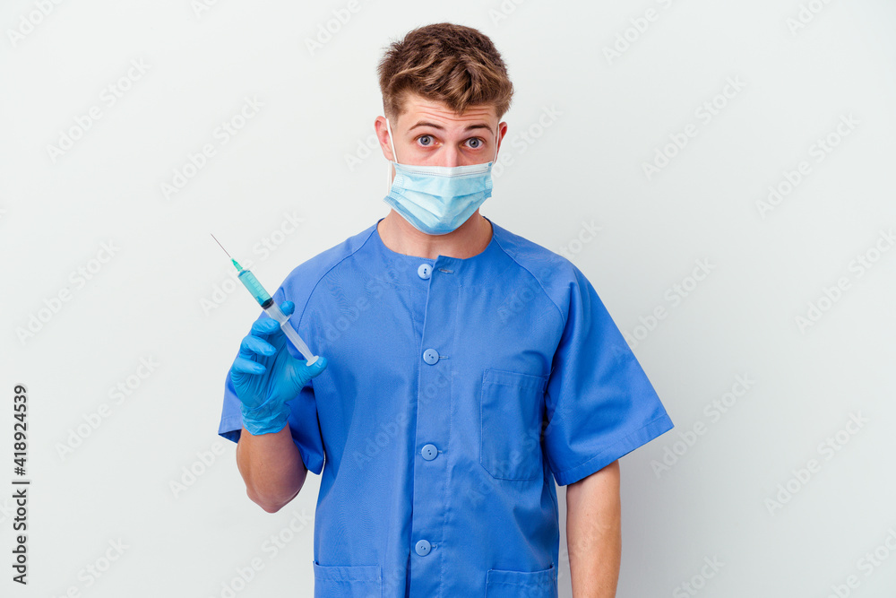 Young caucasian nurse man prepared to give a vaccine isolated on white background shrugs shoulders and open eyes confused. Young caucasian nurse man prepared to give a vaccine isolated on white background shrugs shoulders and open eyes confused.
