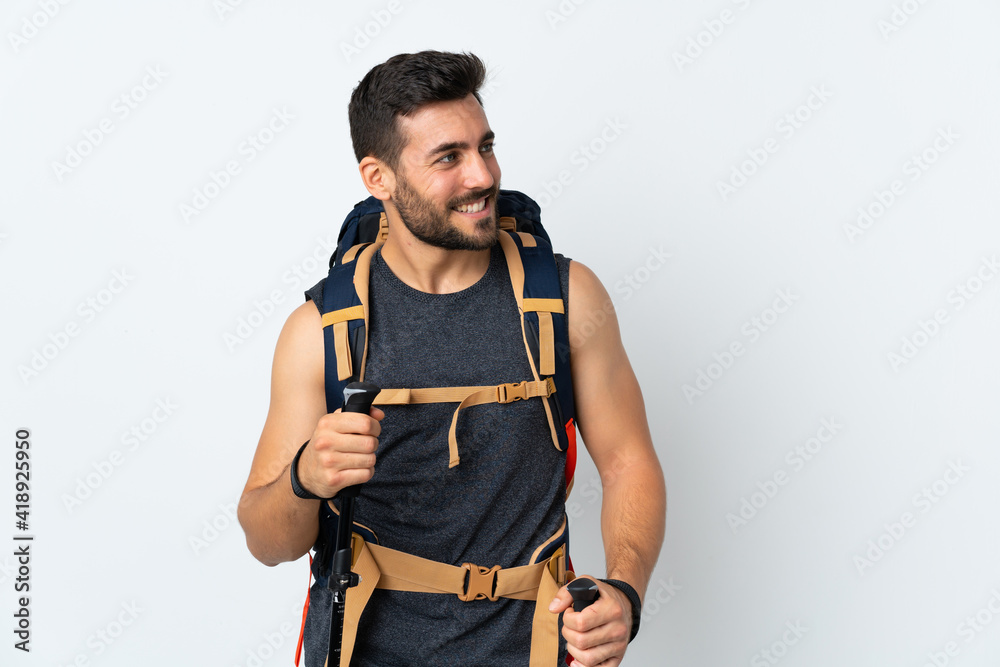 Young mountaineer man with a big backpack and trekking poles isolated on white background looking to the side Young mountaineer man with a big backpack and trekking poles isolated on white background looking to the side