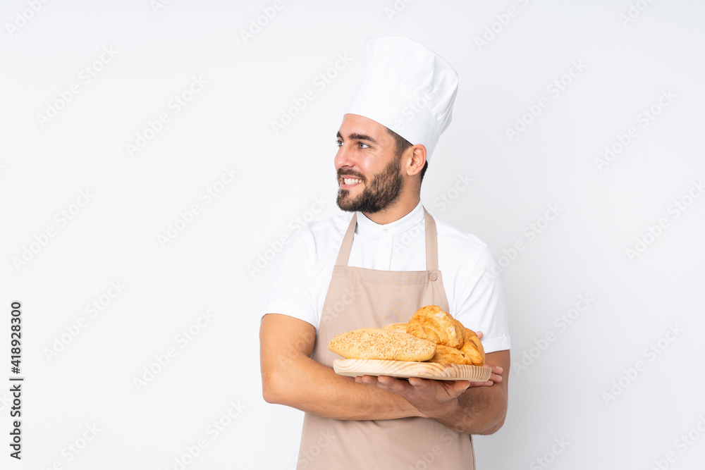 Male baker holding a table with several breads isolated on white background looking to the side Male baker holding a table with several breads isolated on white background looking to the side