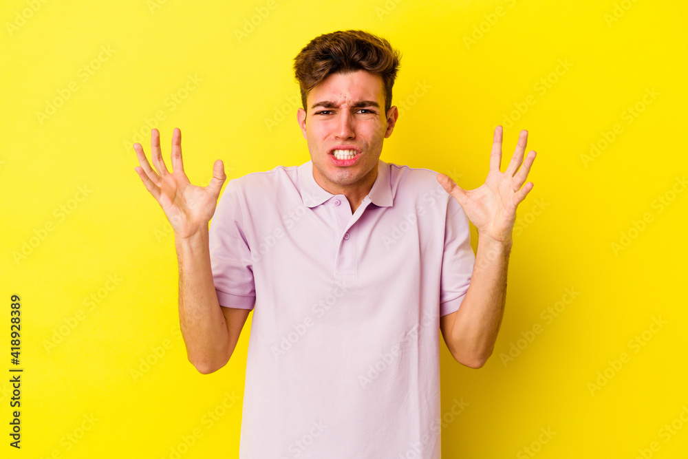 Young caucasian man isolated on yellow background screaming with rage. Young caucasian man isolated on yellow background screaming with rage.