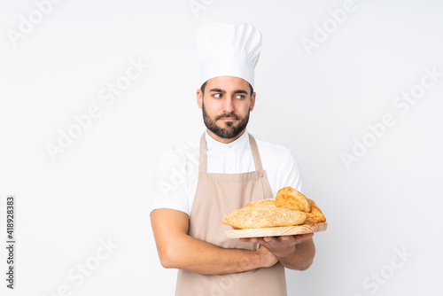 Male baker holding a table with several breads isolated on white background thinking an idea