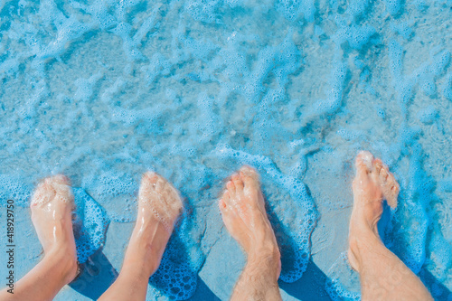 Women's and men's feet stand side by side on the sea beach in blue water, top view