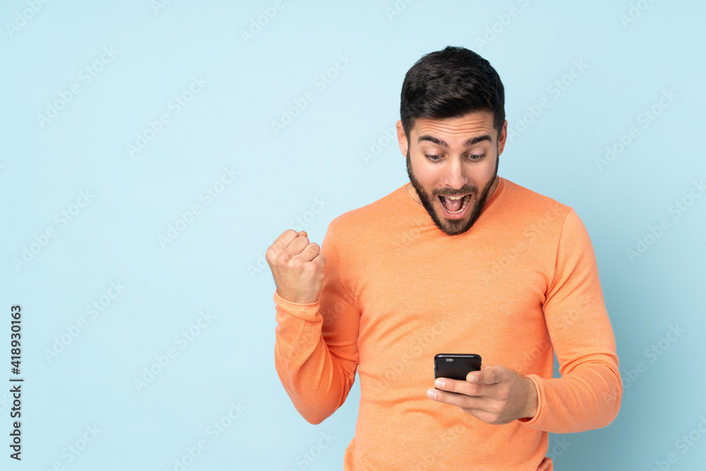 Caucasian handsome man surprised and sending a message over isolated blue background Caucasian handsome man surprised and sending a message over isolated blue background