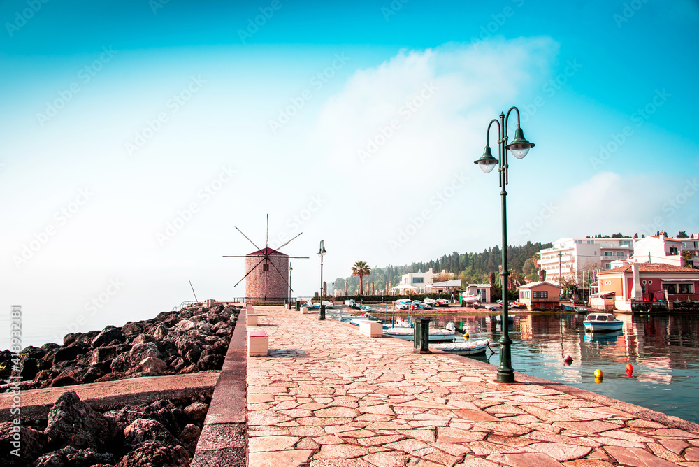 Charming seafront view with stones, lanterns and old windmill on the coast of the Mon Repose area in Kerkira, capital of Corfu, Greece. Amazing places. Popular tourist atraction.