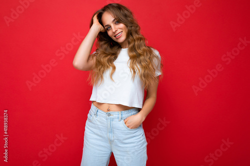 Young beautiful curly blonde woman with sexy expression, cheerful and happy face wearing casual white t-shirt isolated over red background with copy space