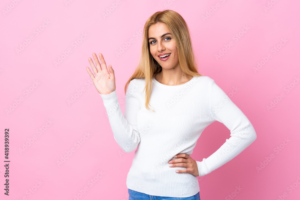 Young Uruguayan blonde woman over isolated pink background saluting with hand with happy expression Young Uruguayan blonde woman over isolated pink background saluting with hand with happy expression