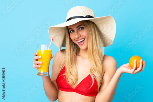 Young Uruguayan blonde woman over isolated blue background in swimsuit and holding a cocktail