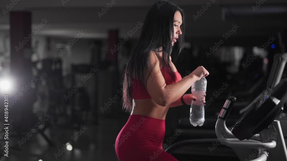 Side view portrait of a sporty girl engaged on a treadmill and drinking water