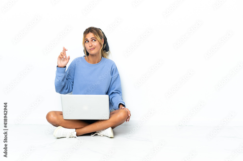 Young blonde Uruguayan girl with the laptop isolated on white background with fingers crossing and wishing the best Young blonde Uruguayan girl with the laptop isolated on white background with fingers crossing and wishing the best