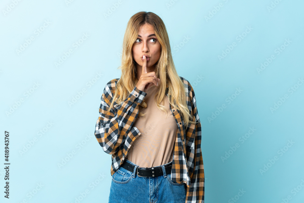Young blonde Uruguayan isolated on blue background showing a sign of silence gesture putting finger in mouth Young blonde Uruguayan isolated on blue background showing a sign of silence gesture putting finger in mouth