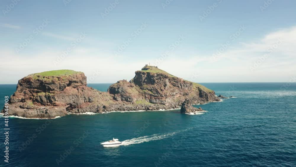 White yacht exploring remote coastline of Ilhéu do Farol in Madeira, aerial White yacht exploring remote coastline of Ilhéu do Farol in Madeira, aerial