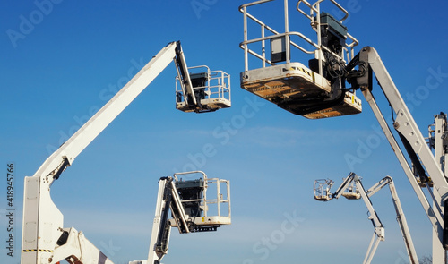 multiple hydraulic telescopic boom lifts or cherry pickers rising into the blue sky