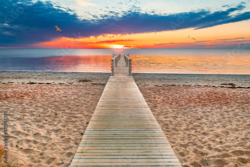Wooden footpath and pier in sandy beach of the Baltic Sea during colorful sun...