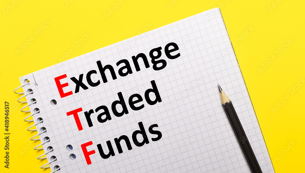 White notebook with inscription Exchange Traded Funds written in black pencil on a bright yellow background. White notebook with inscription Exchange Traded Funds written in black pencil on a bright yellow background.