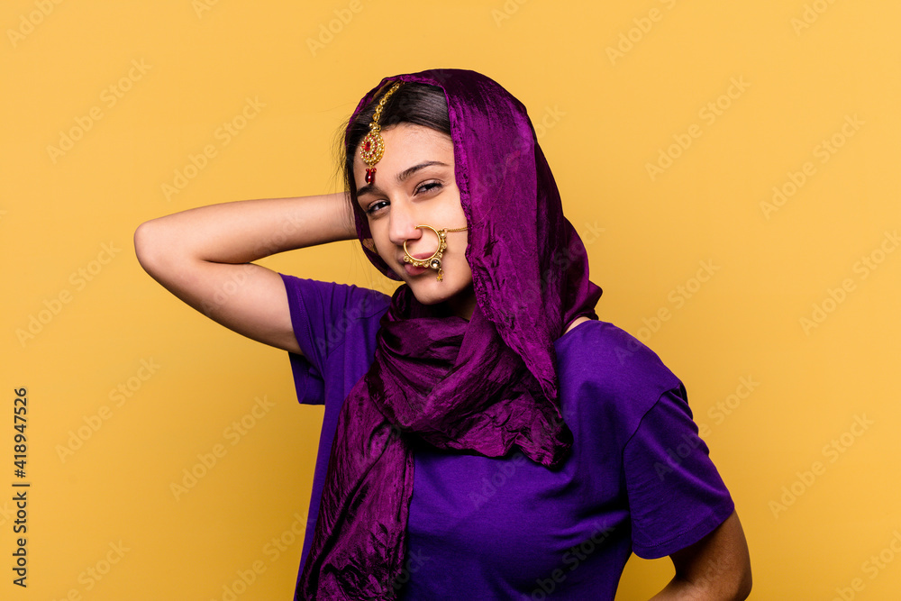 Young Indian woman wearing a traditional sari clothes isolated on yellow background touching back of head, thinking and making a choice.