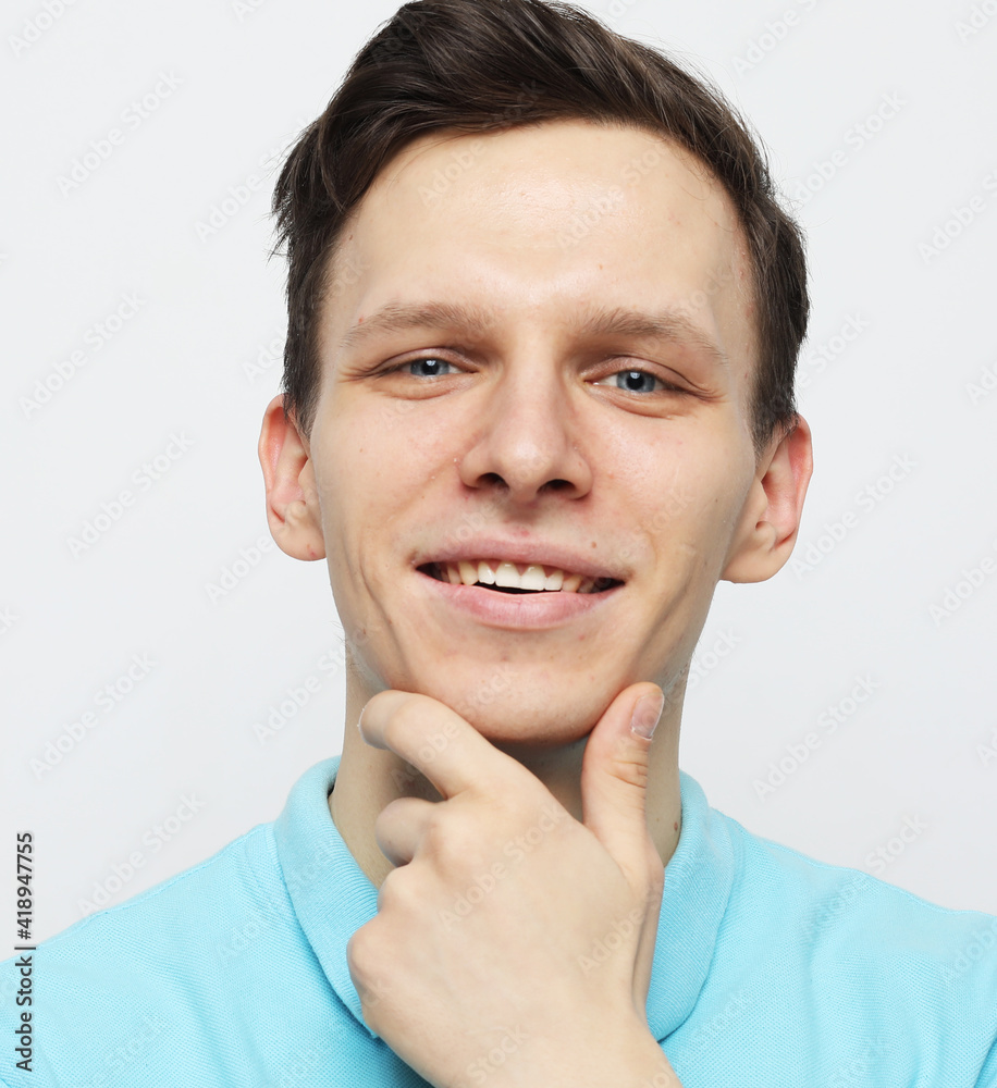 handsome young man smiling and touching his chin over grey background handsome young man smiling and touching his chin over grey background