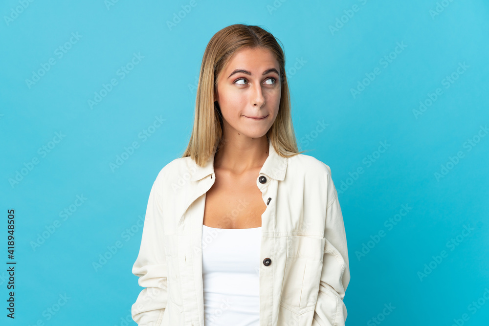 Young blonde woman isolated on blue background having doubts while looking up Young blonde woman isolated on blue background having doubts while looking up