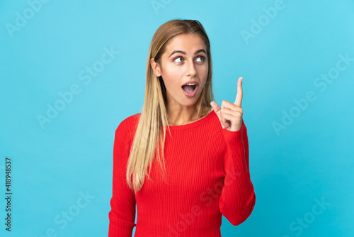 Young blonde woman isolated on blue background thinking an idea pointing the finger up