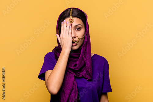 Young Indian woman wearing a traditional sari clothes isolated on yellow background having fun covering half of face with palm. © Asier