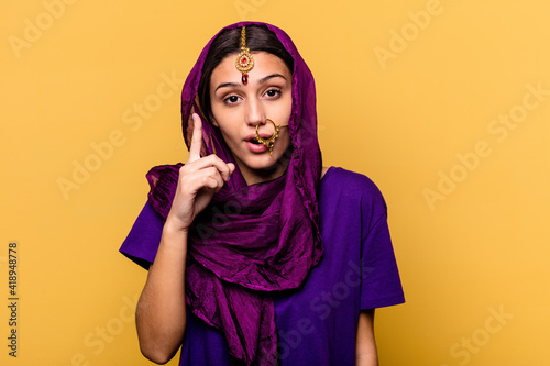 Young Indian woman wearing a traditional sari clothes isolated on yellow background having an idea, inspiration concept. © Asier