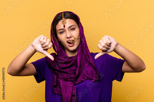 Young Indian woman wearing a traditional sari clothes isolated on yellow background showing thumb down and expressing dislike. © Asier