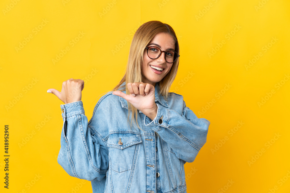 Young blonde woman isolated on yellow background pointing to the side to present a product Young blonde woman isolated on yellow background pointing to the side to present a product