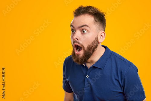 Shocked young man looking away with astonishment in yellow studio photo