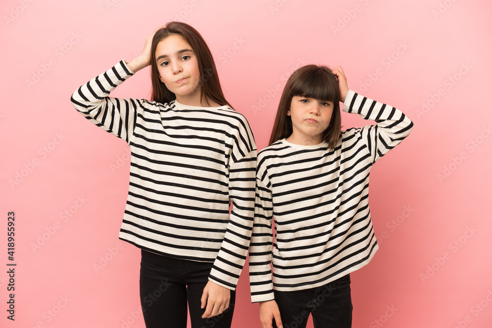Little sisters girls isolated on pink background with an expression of frustration and not understanding Little sisters girls isolated on pink background with an expression of frustration and not understanding