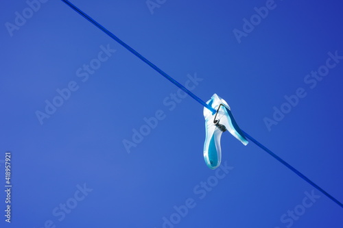 Einzelne blaue Wäschklammer an einer blauen Wäschleine vor blauem Himmel