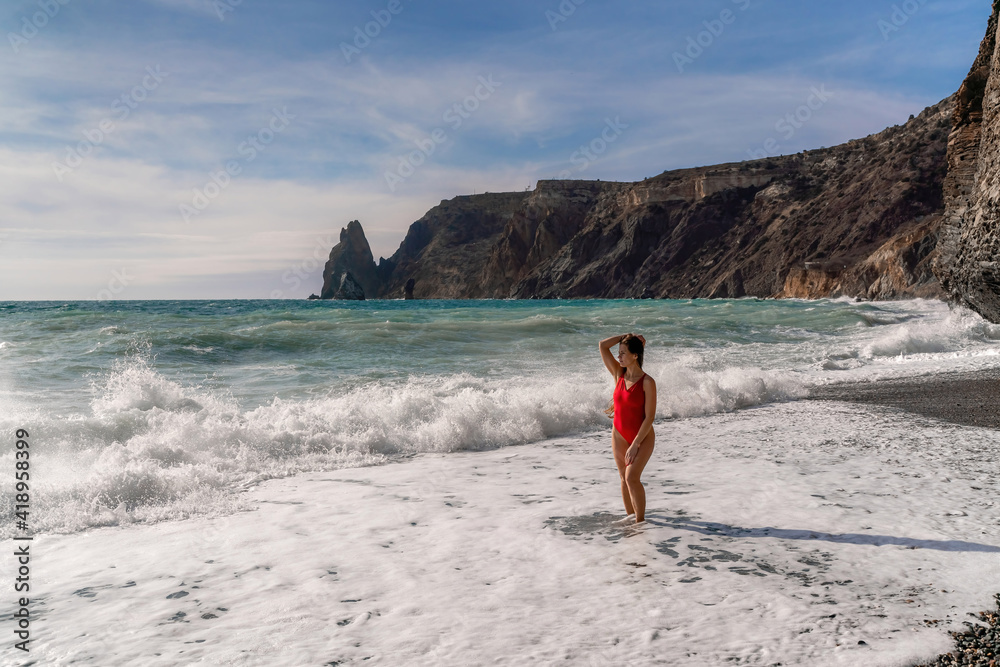 A beautiful and sexy brunette in a red swimsuit on a pebble beach, Running along the shore in the foam of the waves A beautiful and sexy brunette in a red swimsuit on a pebble beach, Running along the shore in the foam of the waves