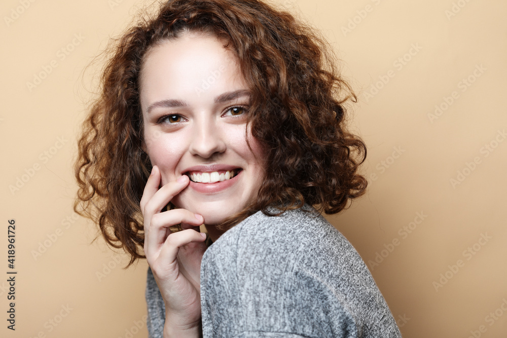 Pretty young woman with cute smile poses alone against beige background. Pretty young woman with cute smile poses alone against beige background.