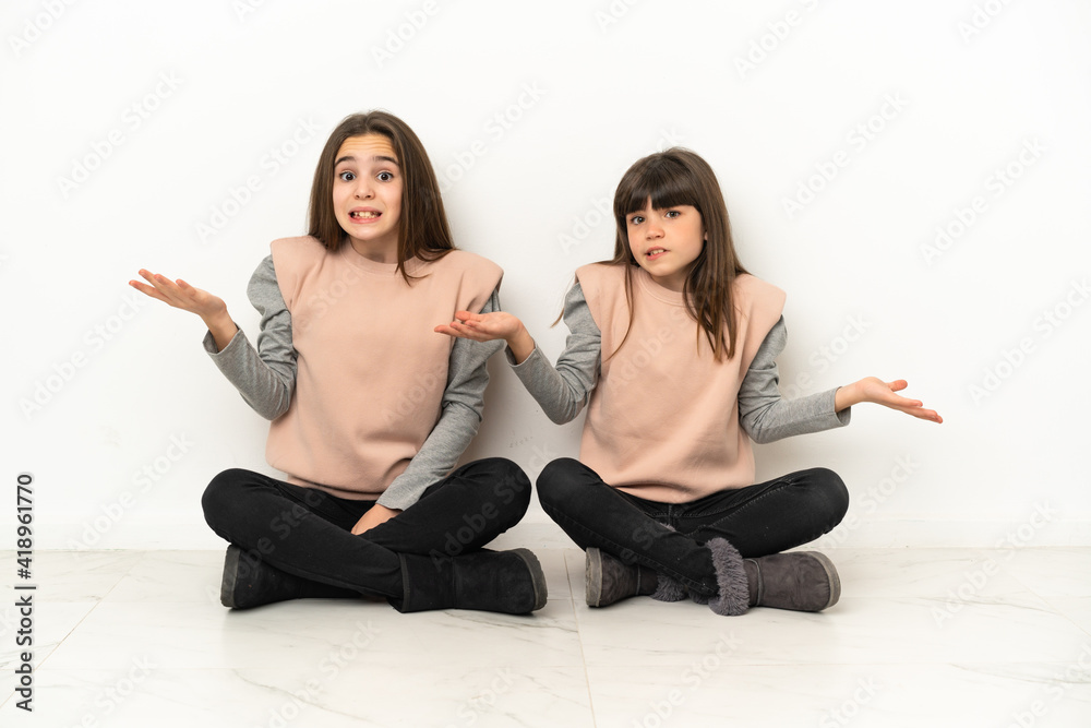 Little sisters sitting on the floor isolated on white background unhappy and frustrated with something because not understand something Little sisters sitting on the floor isolated on white background unhappy and frustrated with something because not understand something