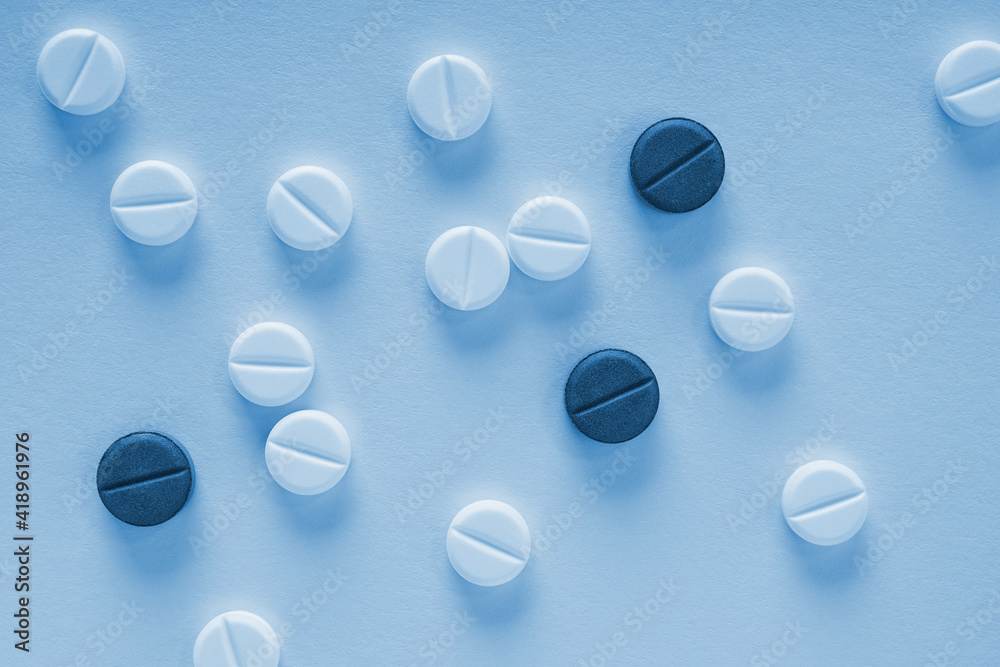 Blue tinted background or backdrop on the theme of medicine, health care, drugs, pharmacology. Light and dark pills lie on a sheet of paper. Close-up. Top view from above. Macro Blue tinted background or backdrop on the theme of medicine, health care, drugs, pharmacology. Light and dark pills lie on a sheet of paper. Close-up. Top view from above. Macro