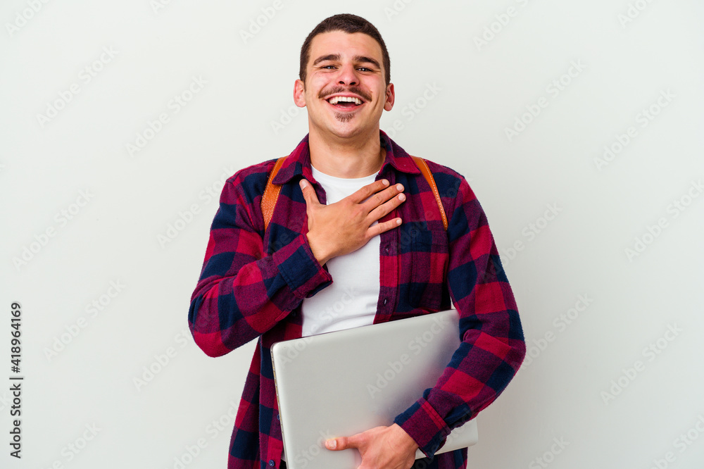 Young caucasian student man holding a laptop isolated on white background laughs out loudly keeping hand on chest. Young caucasian student man holding a laptop isolated on white background laughs out loudly keeping hand on chest.