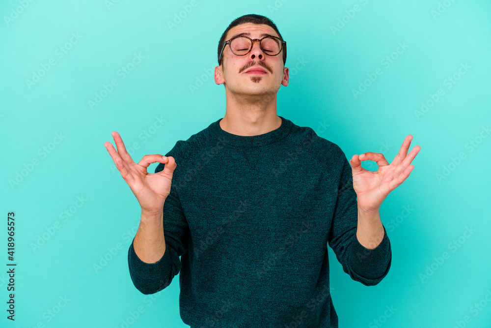 Young caucasian man isolated on blue background relaxes after hard working day, she is performing yoga. Young caucasian man isolated on blue background relaxes after hard working day, she is performing yoga.