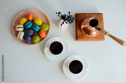 Two cup of coffee, multicolored macaroons, turkish coffee pot on white background, top view