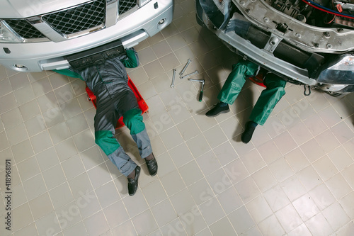 фотографія Mechanics in uniform lying down and working under car at the garage